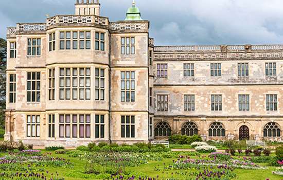 A grand mansion with three storeys beyond a green lawn and colourful flowers