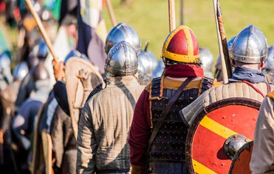 Soldier reenactors wearing armour stand in a field with thier backs turned in a field at Battle Abbey.