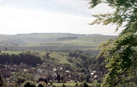 A view from the hills looking down on the village of Eyam, which is surrounded by fields and greenery.