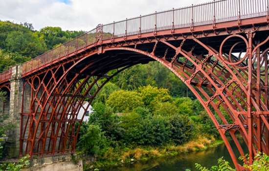 A close-up view of the Iron Bridge in Shropshire over the river. Someone is kayaking underneath the bridge's arch.