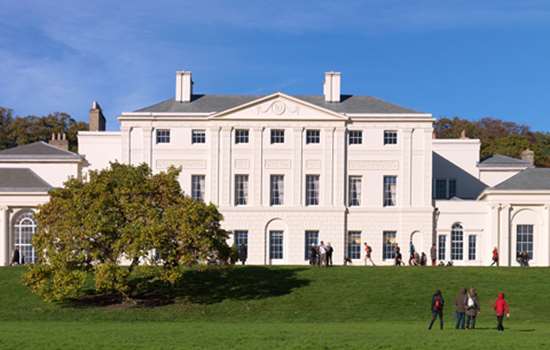 A view of the facade of Kenwood House with people walking in front of the building. 
