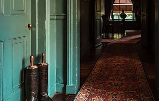 A corridor in a grand building with a pair of boots by a green door