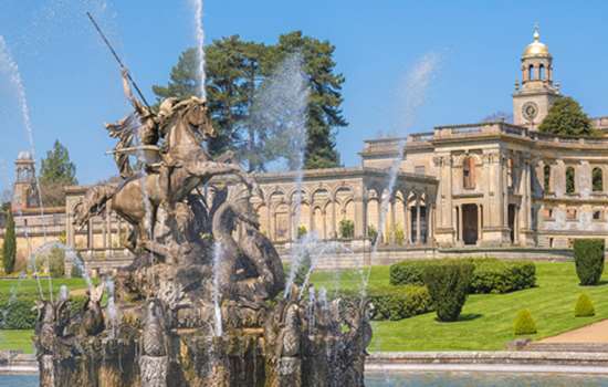 A view of Witley Court ruins on a sunny day and the water fountain in the foreground.