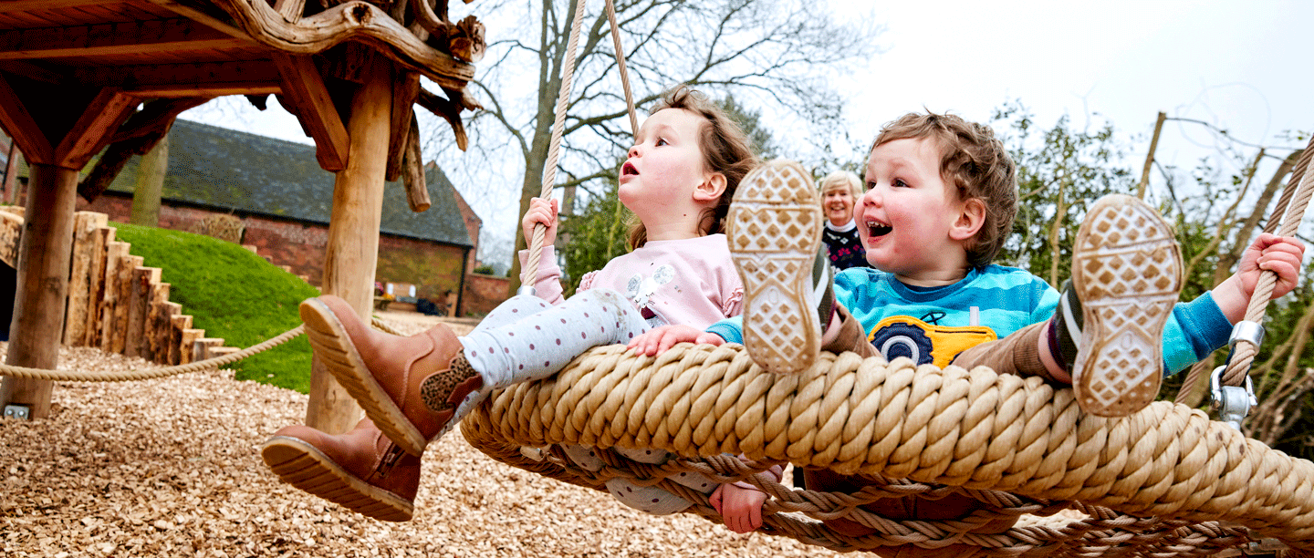 Image: children are playing on a large round swing in the play area